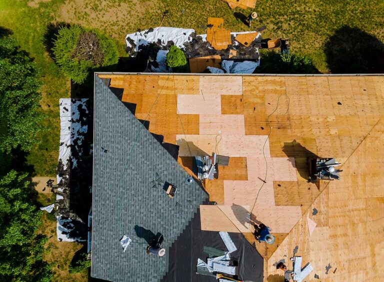 Close-up of a roofer inspecting metal roofing panels beside architectural asphalt shingles.
