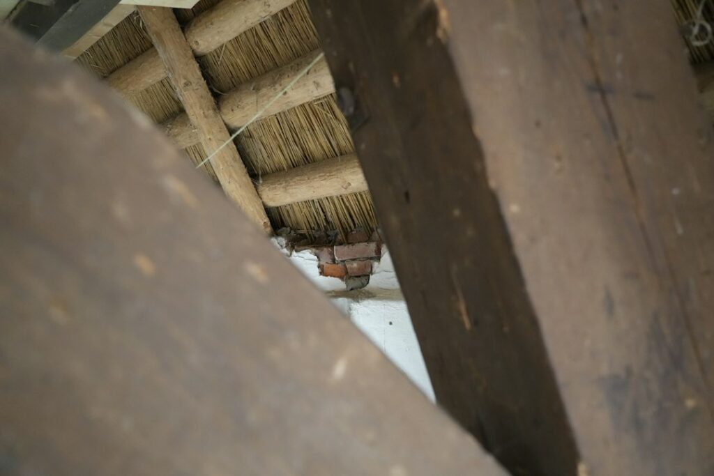 A homeowner examines water-stained roof framing and damp insulation in a dim attic with a flashlight.