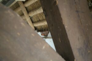 A homeowner examines water-stained roof framing and damp insulation in a dim attic with a flashlight.