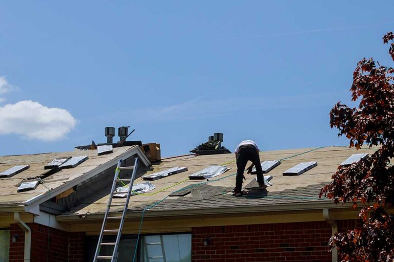 A homeowner examines a damaged roof vent and small attic entry gap with a flashlight.